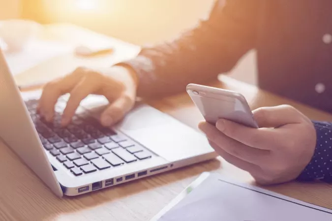 Une personne devant un ordinateur avec un téléphone portable